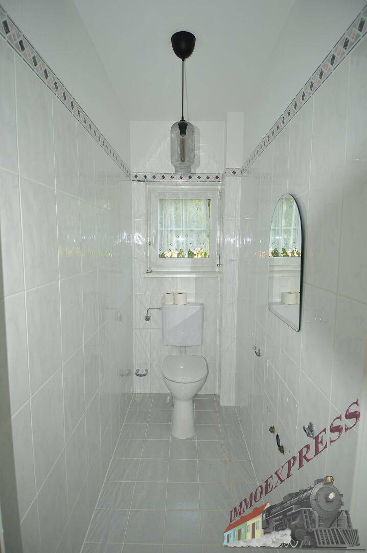 Kleines Gäste-WC mit Fenster, weißen Fliesen und einer einfachen Toilette.