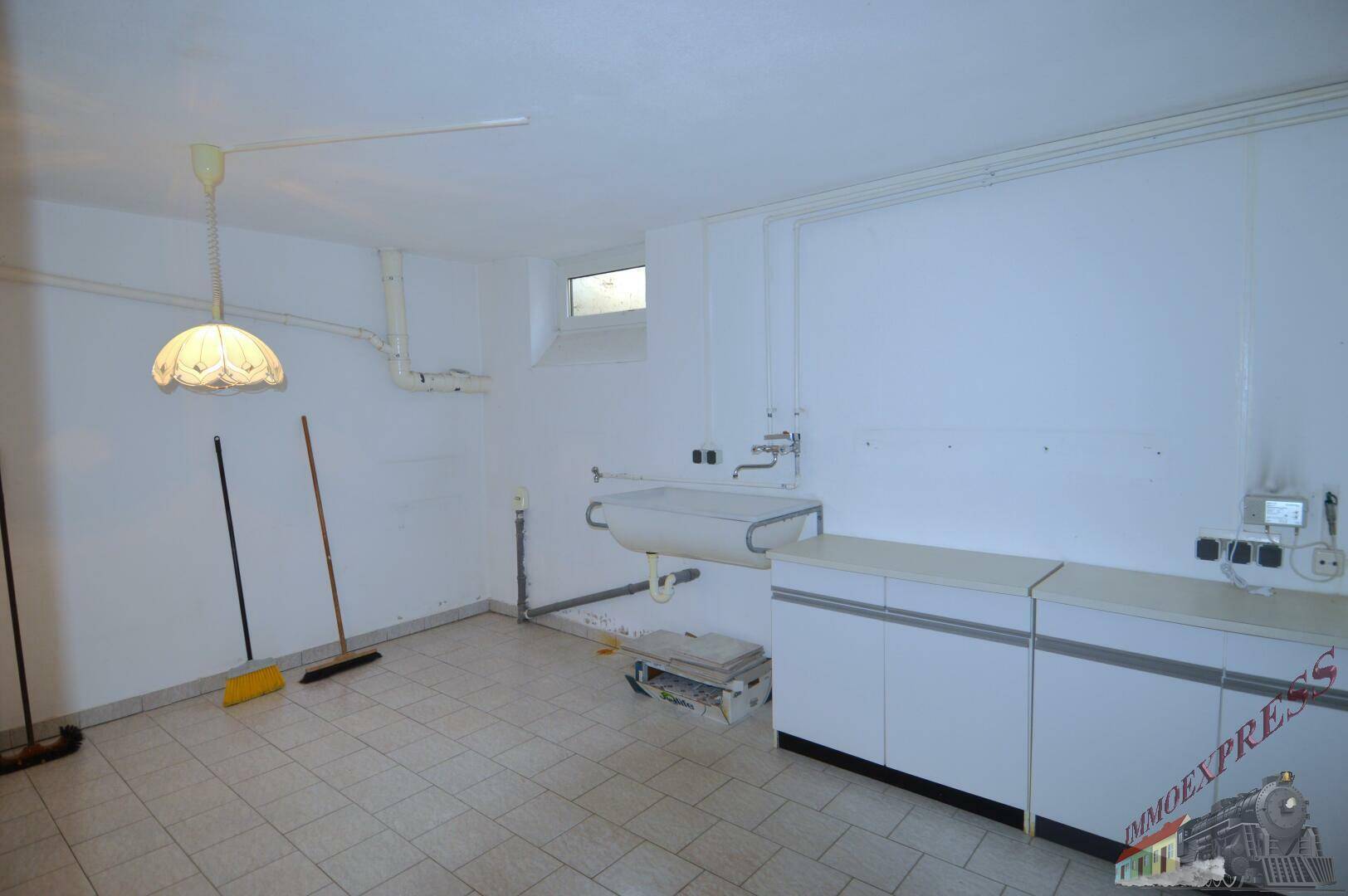 Hauswirtschaftsraum im Keller mit Waschbecken, Unterschränken und Fliesenboden.