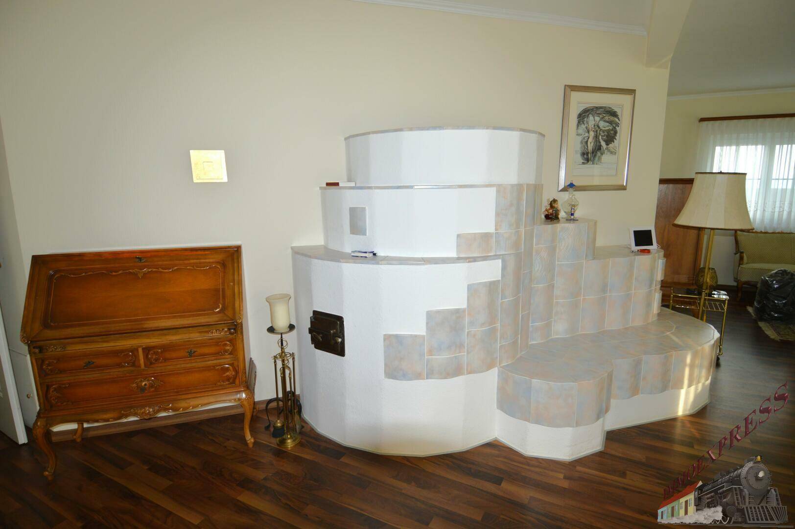 Gemütliches Wohnzimmer mit Holzboden und einem großen, traditionellen Kachelofen als Blickfang.