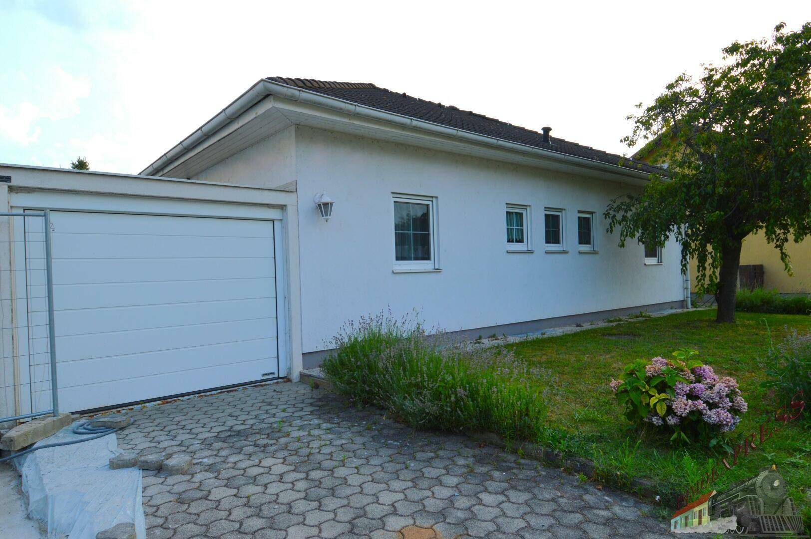 Seitenansicht des Hauses mit integrierter Garage und gepflasterter Einfahrt.