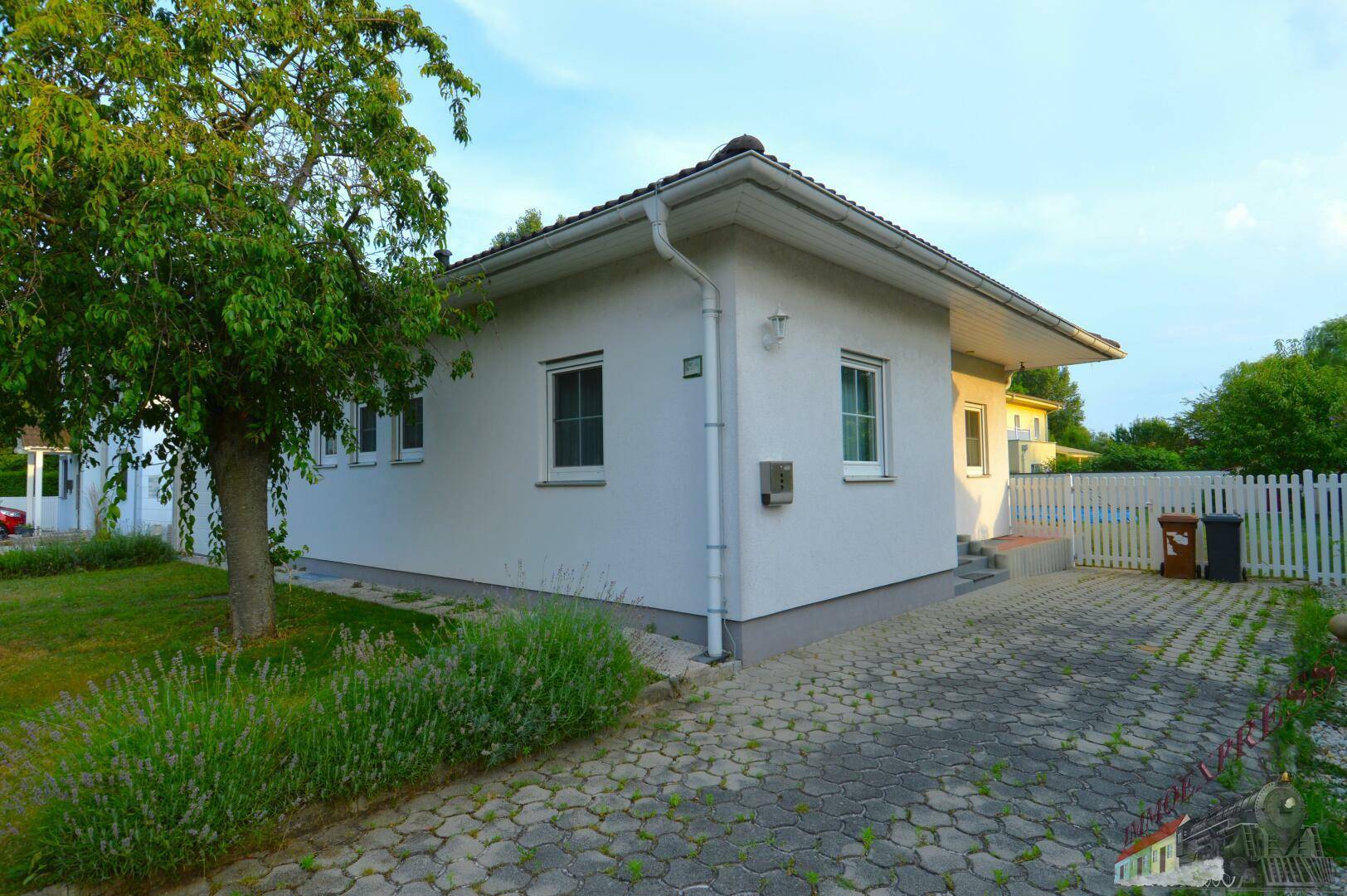 Vorderansicht des Hauses mit gepflasterter Einfahrt, kleinem Vorgarten und weißem Zaun.