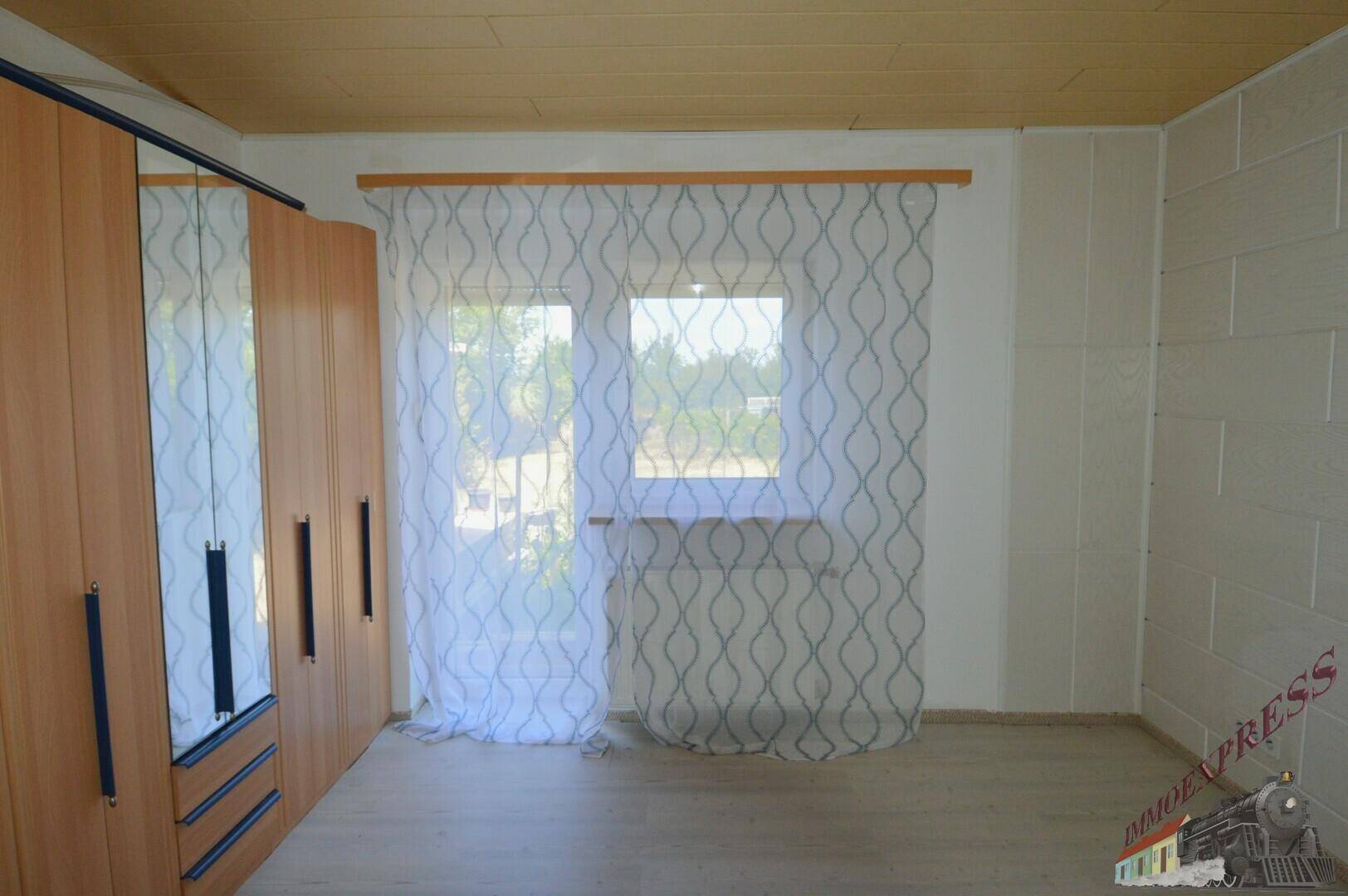 Schlafzimmer mit Einbauschrank, hellem Laminatboden und Fenster.