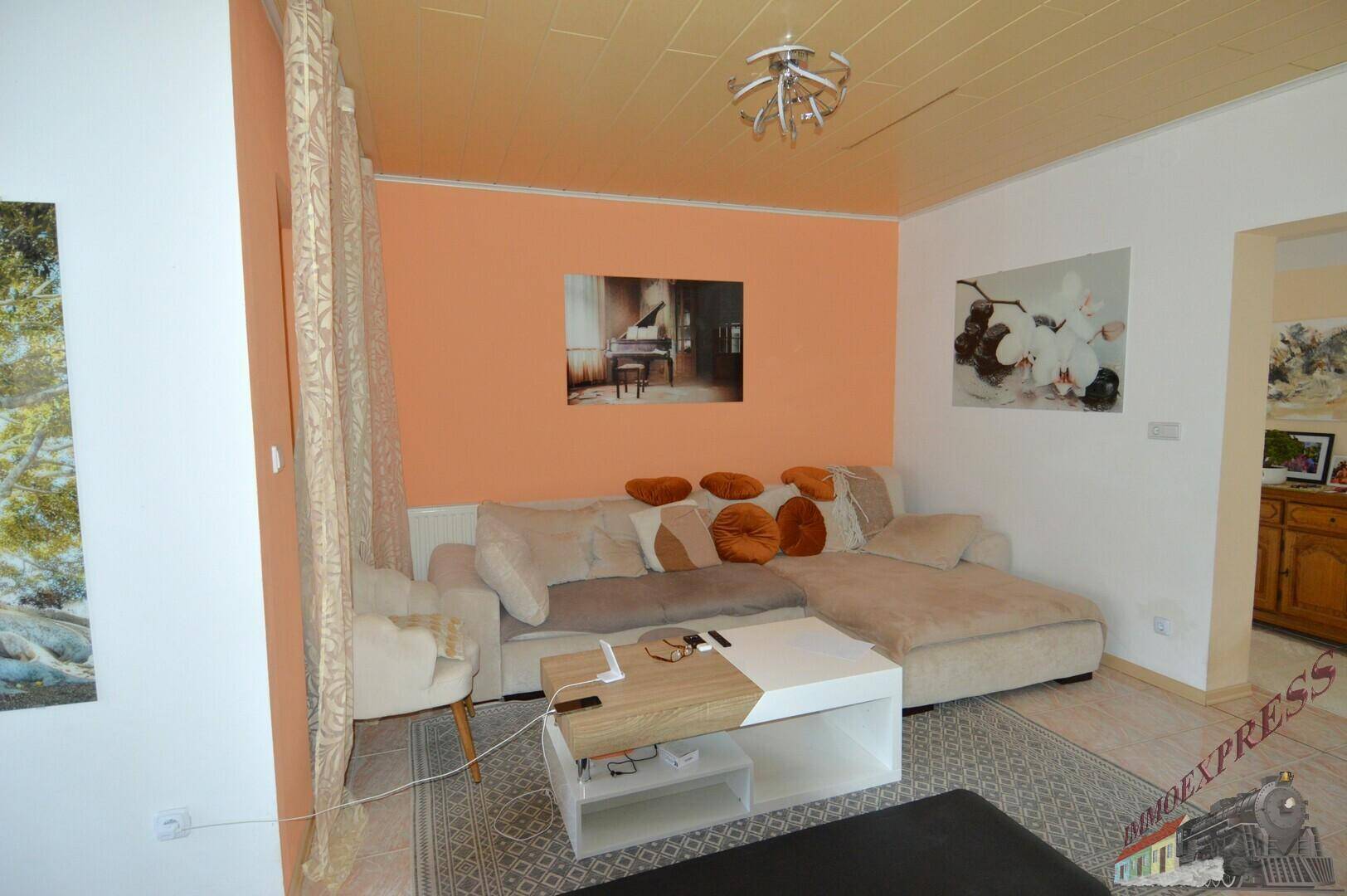 Wohnzimmer mit beigem Sofa, Couchtisch und orangefarbener Akzentwand.