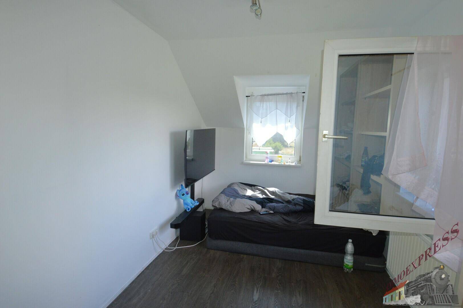 Kleines Schlafzimmer im Dachgeschoss mit Bett, Fernseher und Fenster.