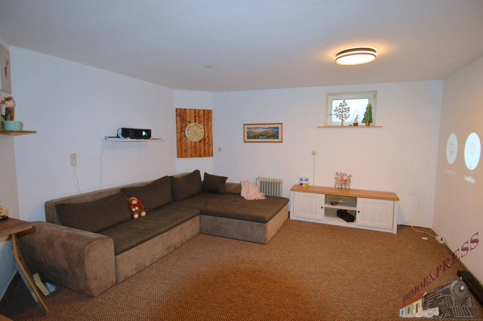 Wohnzimmer mit großem Ecksofa, kleinem Fenster und Medienkonsole.