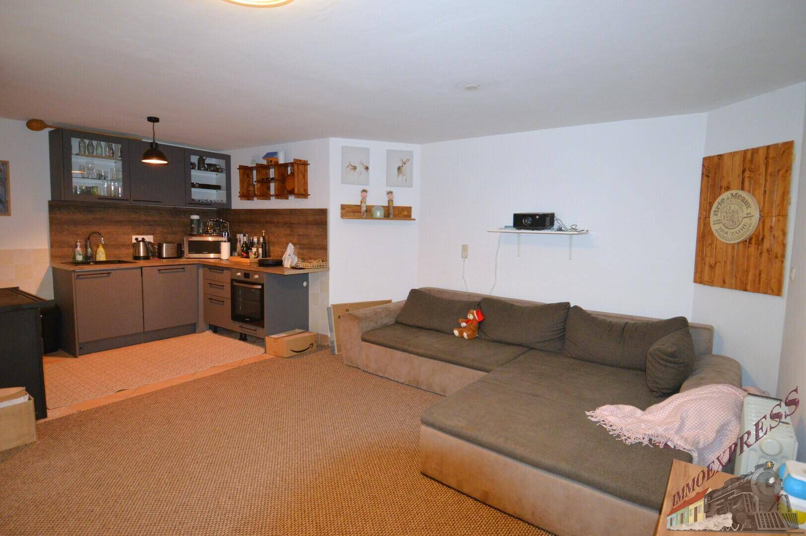Gemütliches Wohnzimmer mit großem Ecksofa und integrierter kleiner Küchenzeile.