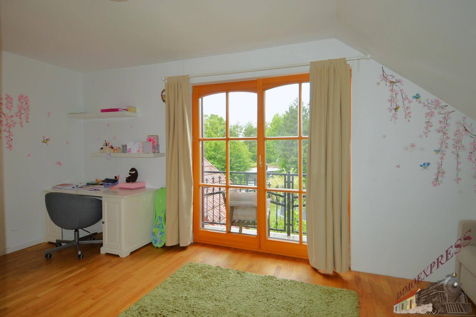 Arbeitszimmer mit Schreibtisch, Holzboden und Balkonzugang mit Blick ins Grüne.