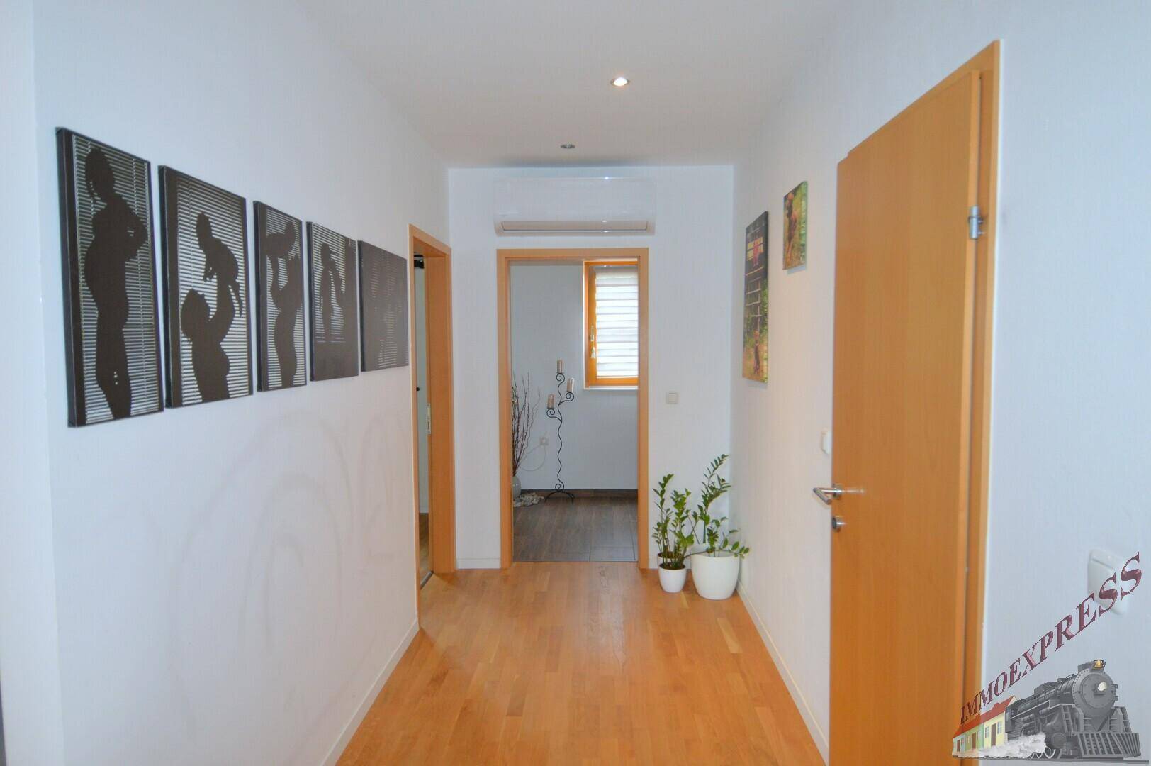 Heller Flur mit Holzboden, weißen Wänden und dekorativen Bildern.