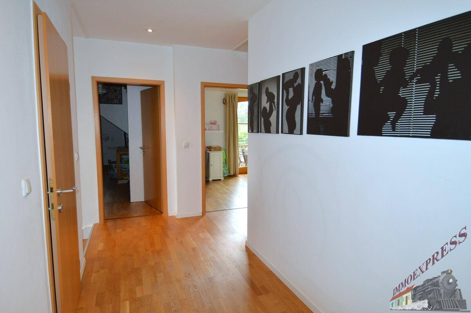 Heller Flur mit Holzboden, weißen Wänden und dekorativen Bildern.