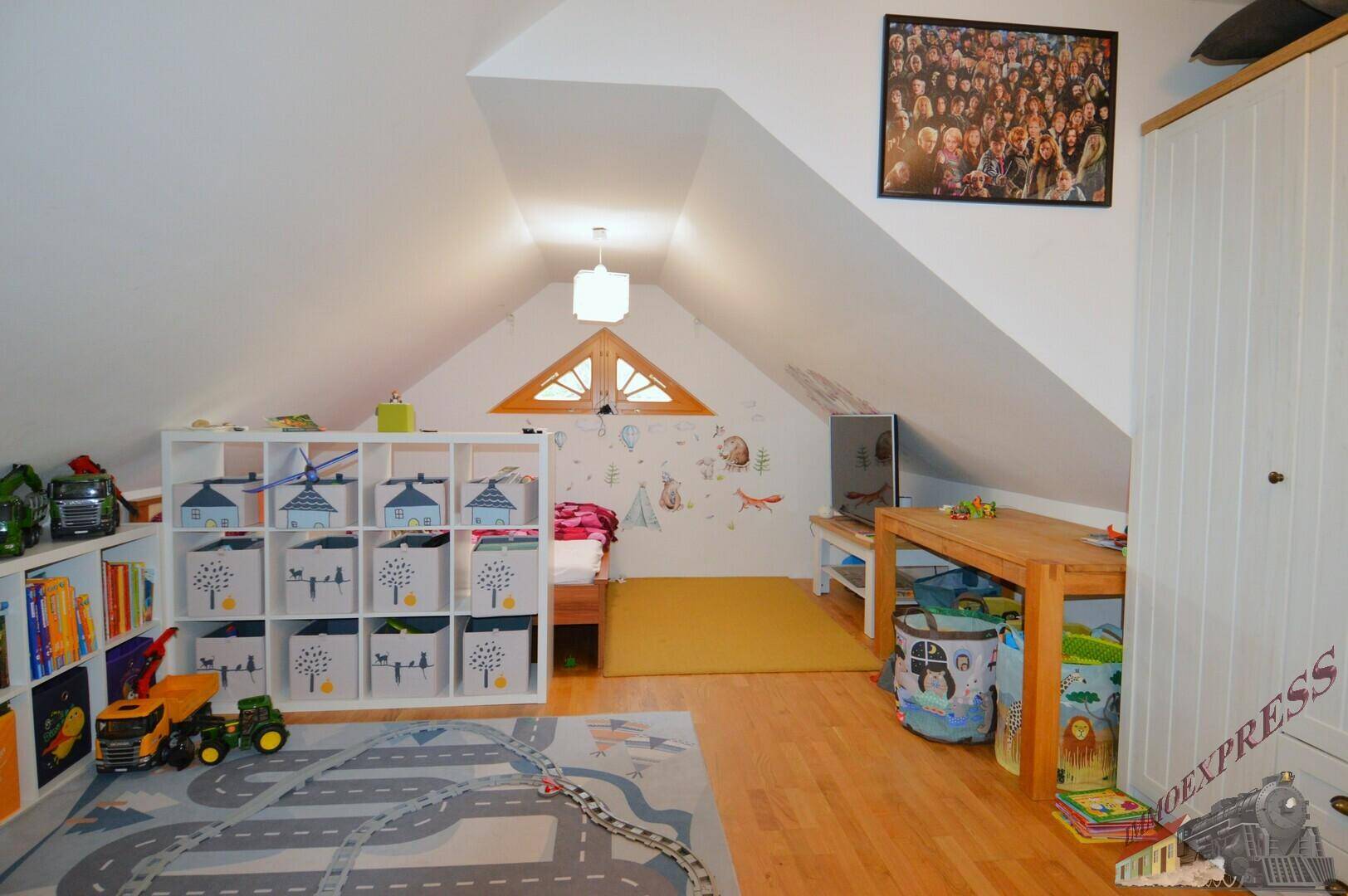 Geräumiges Kinderzimmer mit Spielzeug, Regalen und einem dreieckigen Fenster im Dachgeschoss.
