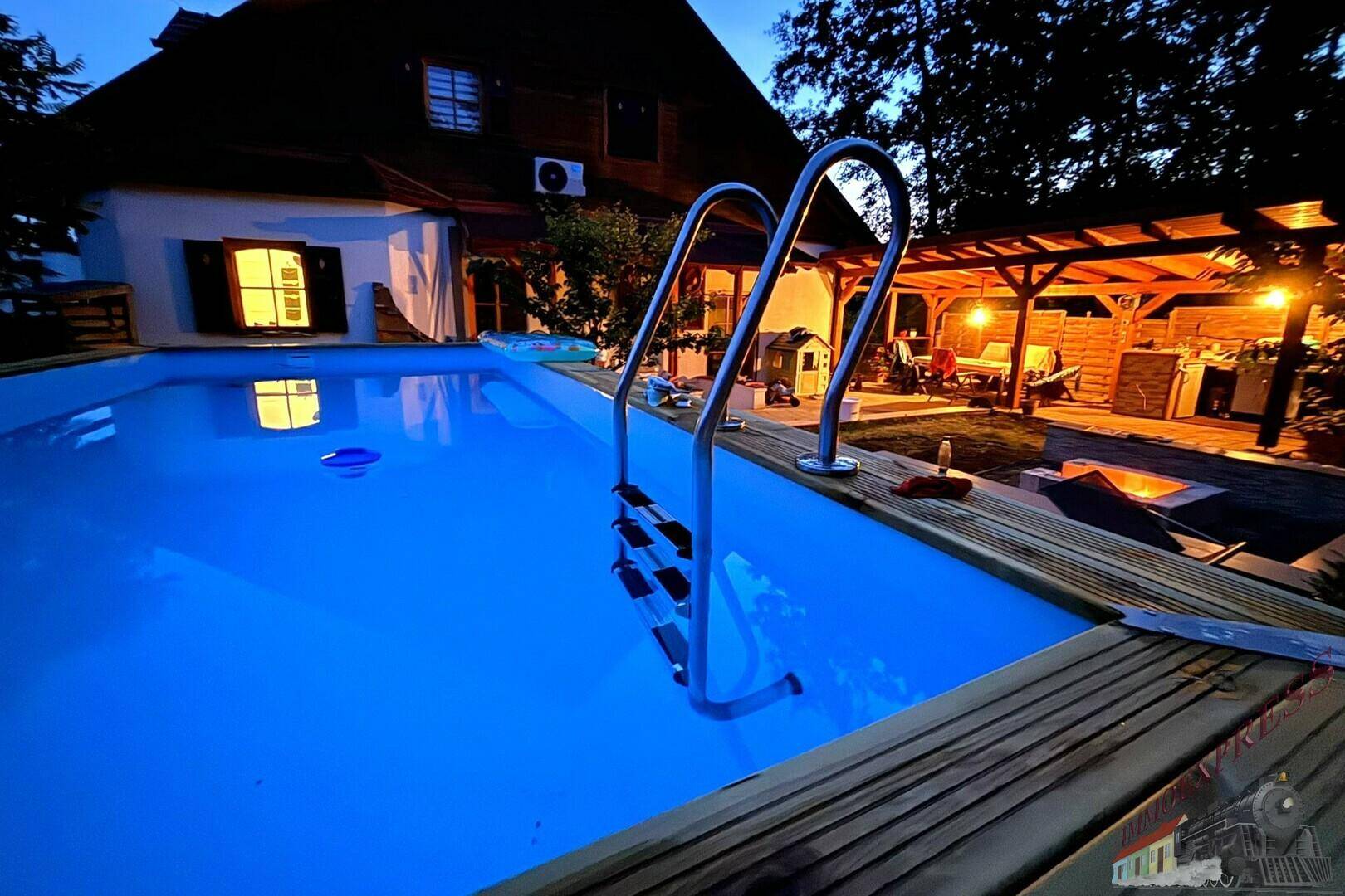 Beleuchteter Außenpool bei Nacht mit Blick auf das gemütliche Haus und den Gartenbereich.
