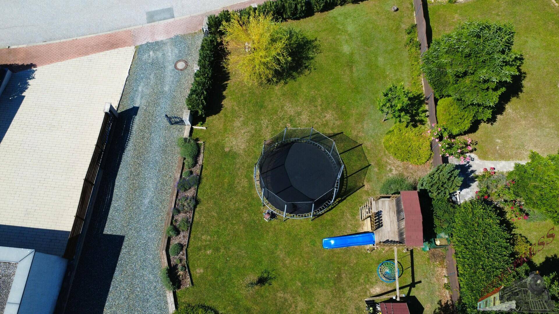 Luftaufnahme des gepflegten Gartens mit Trampolin, Spielplatz und Rasenfläche neben der Auffahrt.