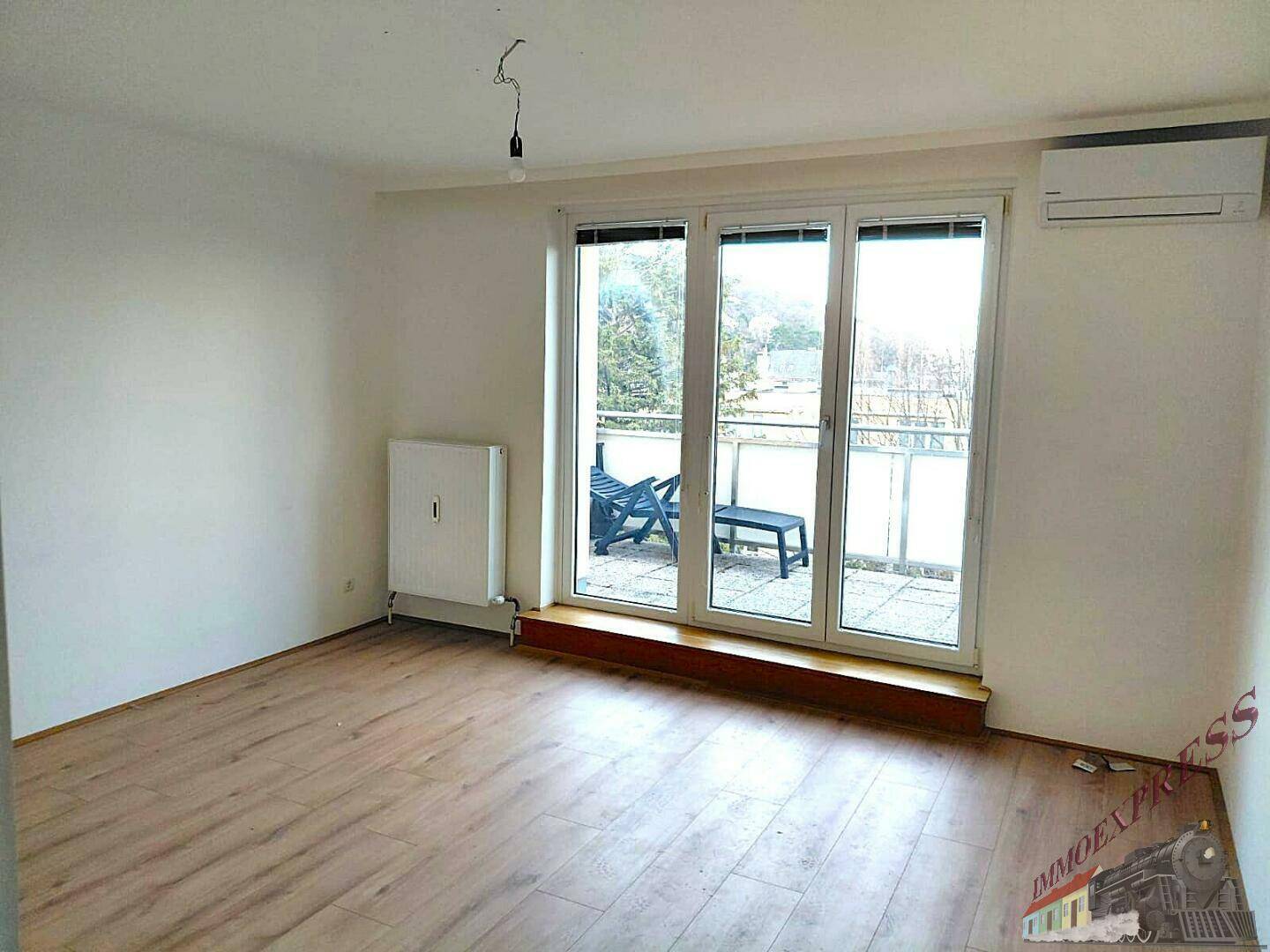Lichtdurchfluteter Raum mit Laminatboden, Klimaanlage und Blick auf den möblierten Balkon.