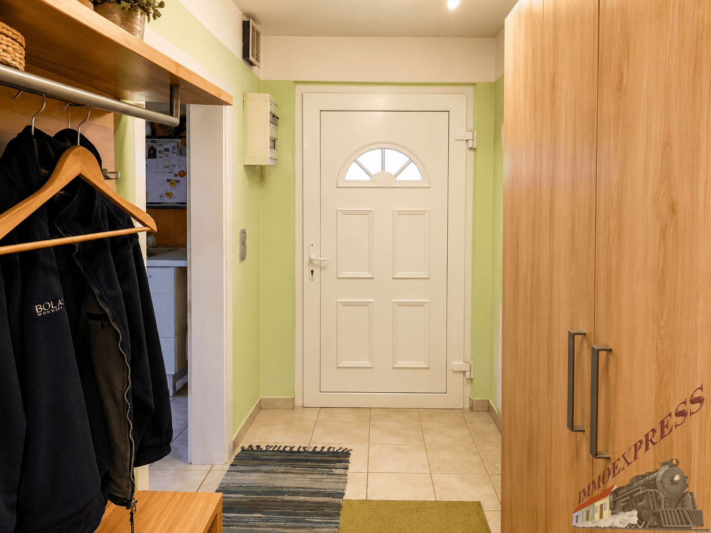 Heller Flur mit weißer Eingangstür, Holzgarderobe und hellgrünen Wänden.