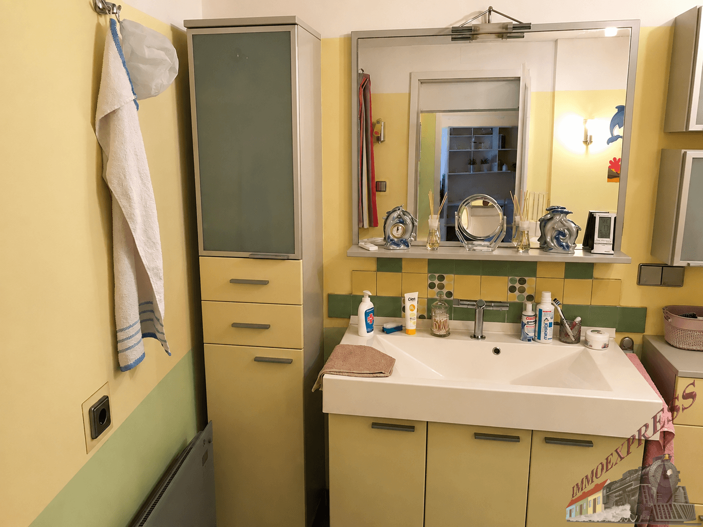 Badezimmer mit Waschbecken, großem Spiegel und gelb-grünen Fliesen im Retro-Stil.
