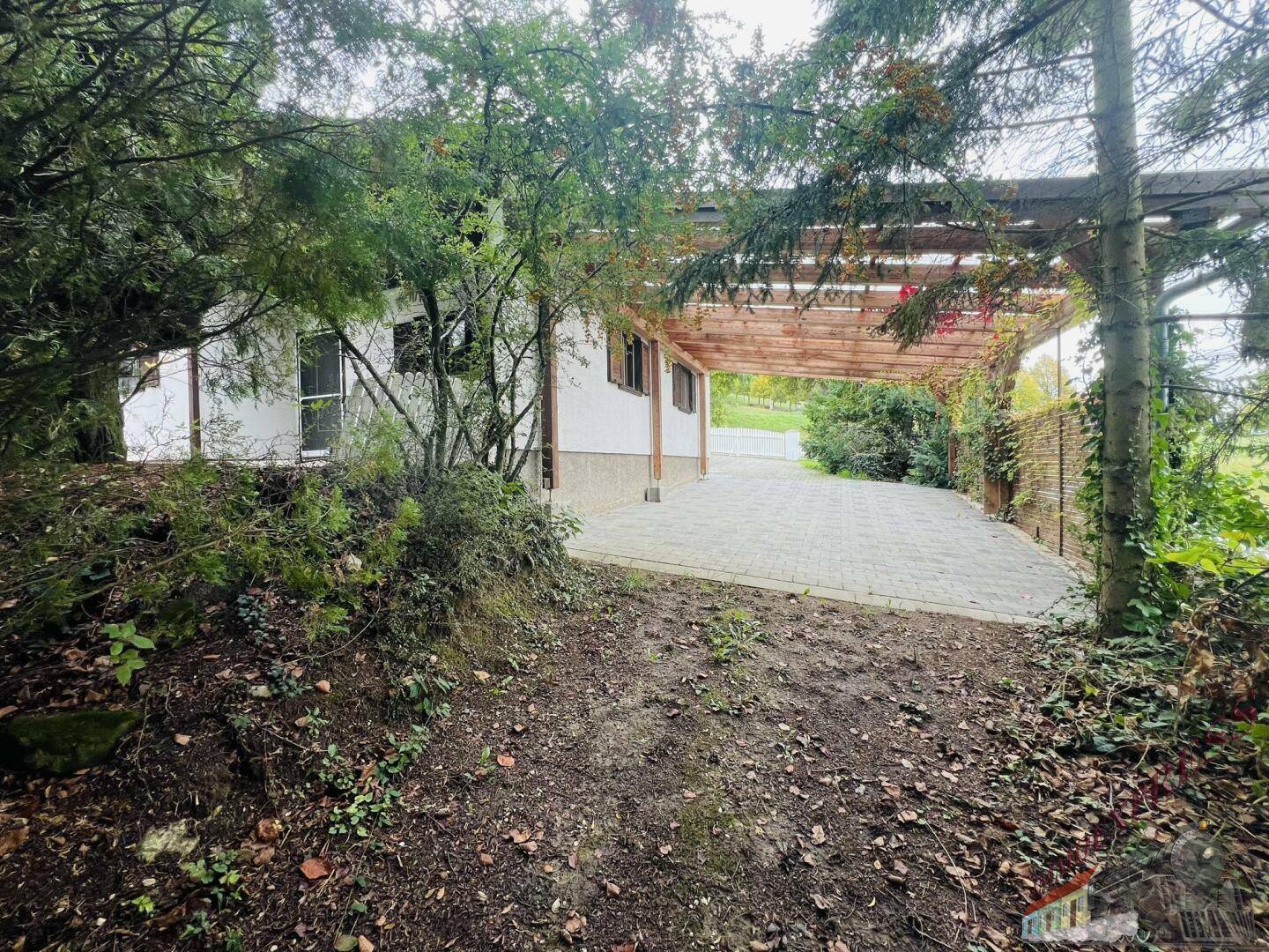 Überdachter Stellplatz oder Terrasse, umgeben von dichter Vegetation und Bäumen.