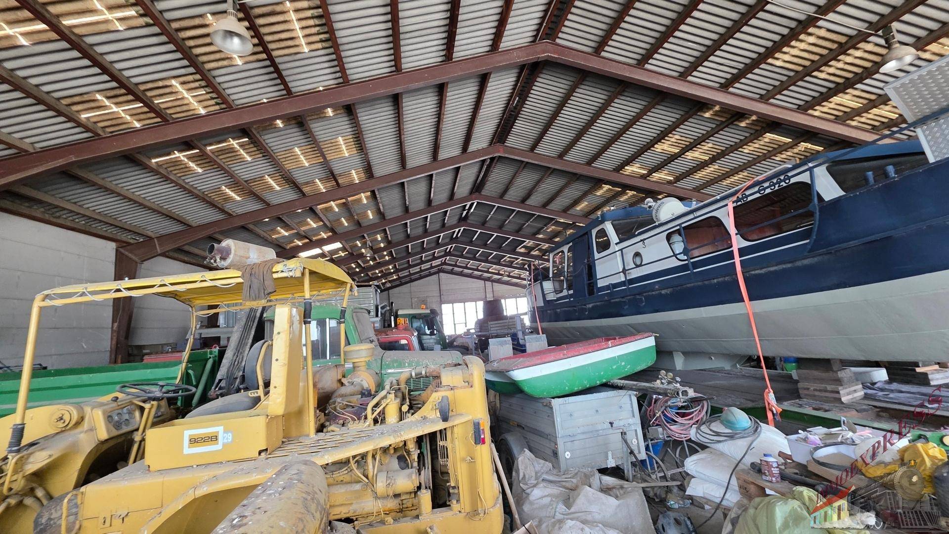 Große Lagerhalle mit hoher Decke, sichtbaren Metallträgern und verschiedenen Fahrzeugen und Booten.