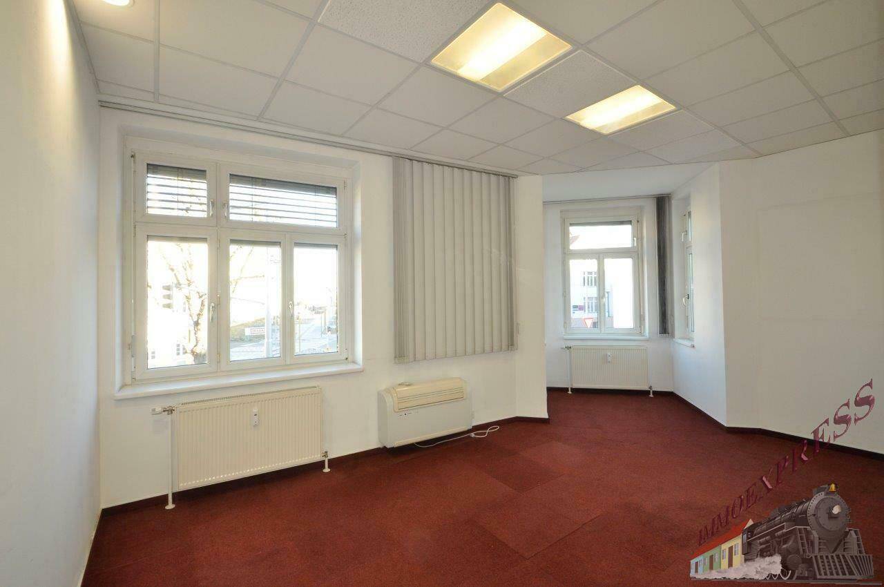 Großes Eckbüro mit rotem Teppichboden, mehreren Fenstern mit Jalousien und Heizkörpern für angenehme Wärme.