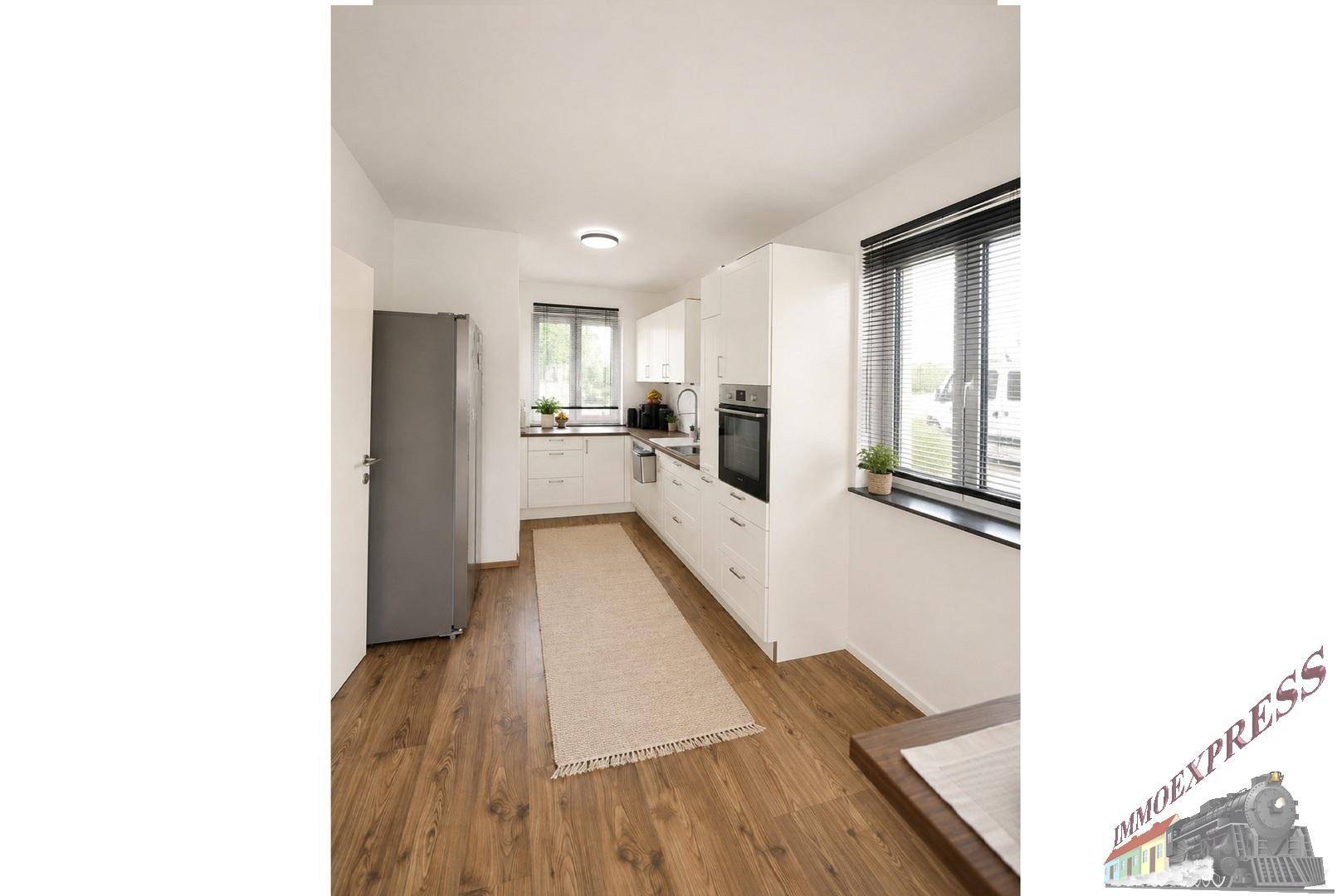 Helle Küche mit modernen weißen Schränken, integrierten Geräten und Holzboden.