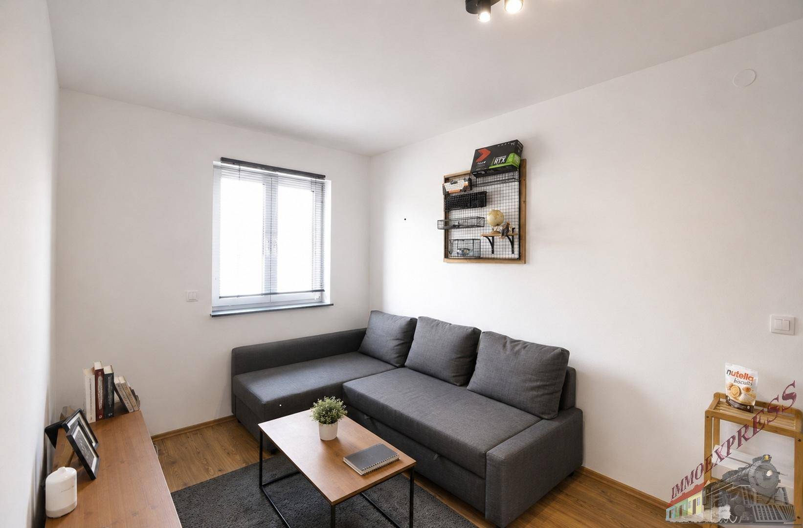 Gemütliches Wohnzimmer mit grauem Ecksofa, Holzboden und Fenster.