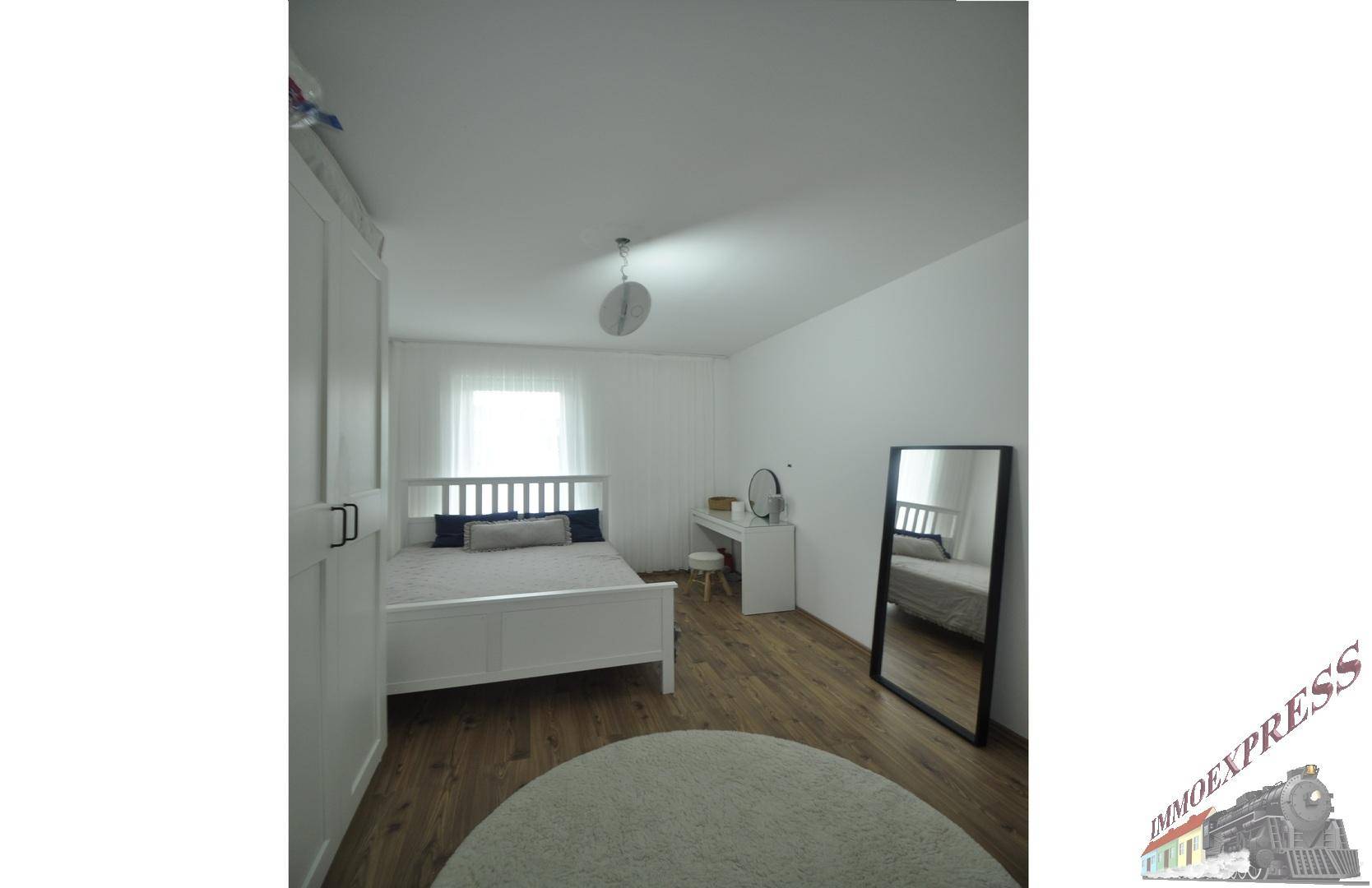 Schlafzimmer mit weißer Einrichtung, Holzboden und viel Tageslicht.