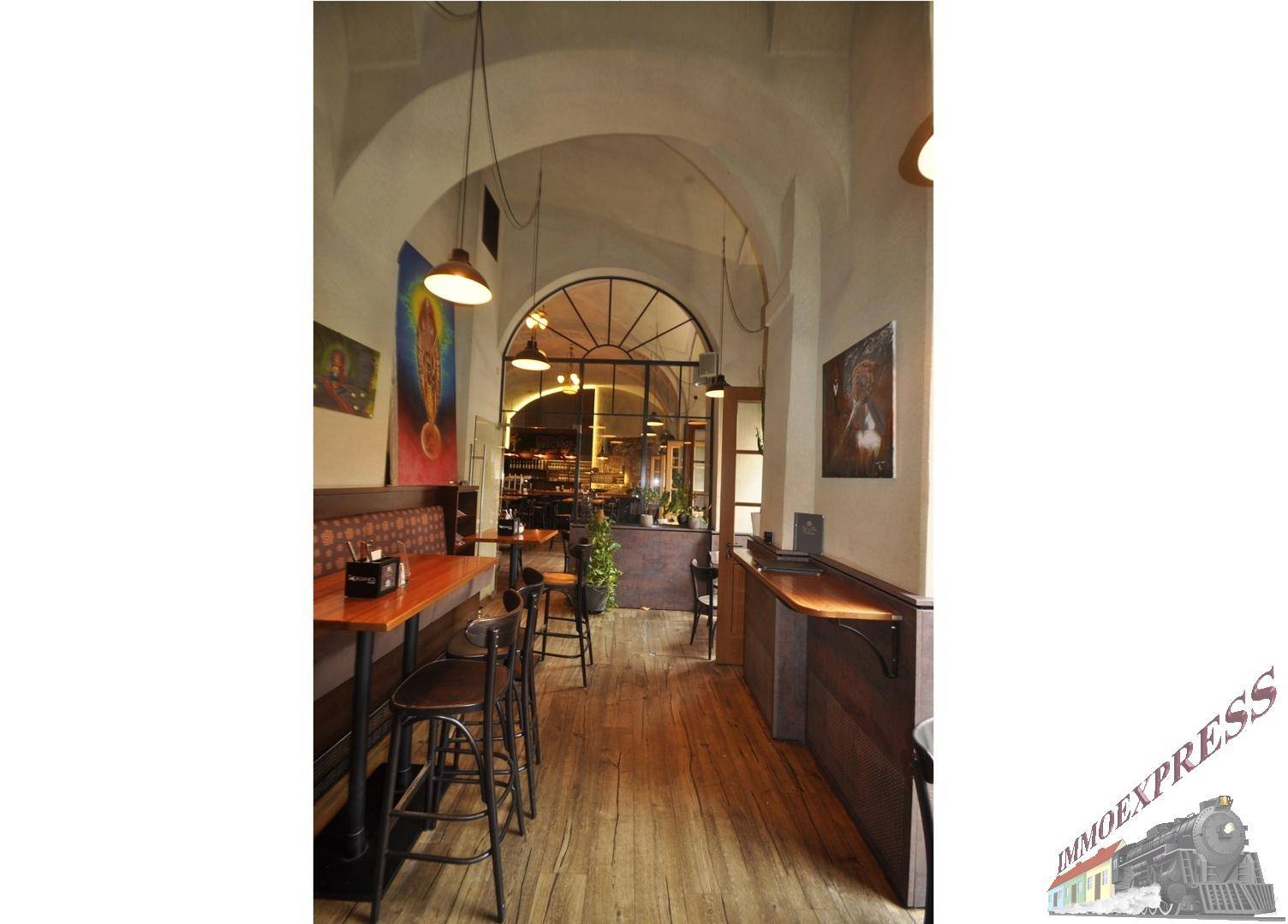Restaurantbereich mit Holzboden, Sitzbänken und einem großen, bogenförmigen Fenster am Ende des Raumes.