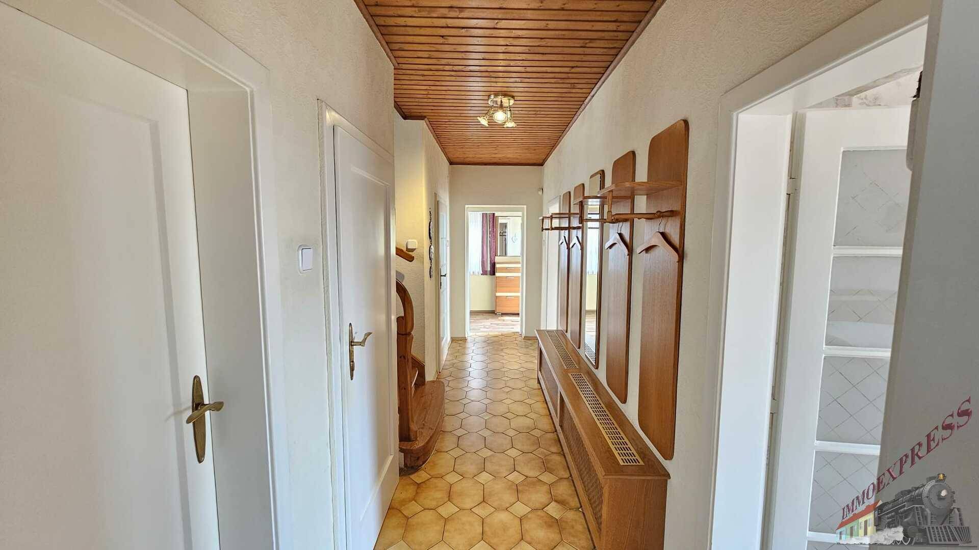 Langer Flur mit Holzdecke, Fliesenboden und traditioneller Garderobe.