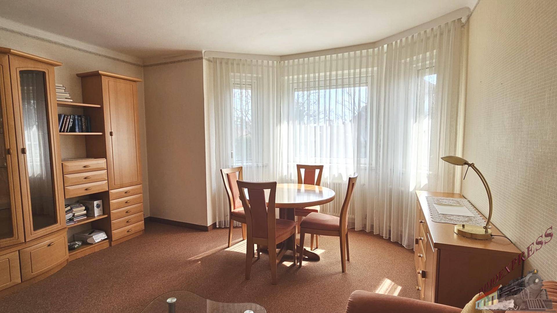Heller Essbereich mit rundem Holztisch und Stühlen, umgeben von großen Fenstern.