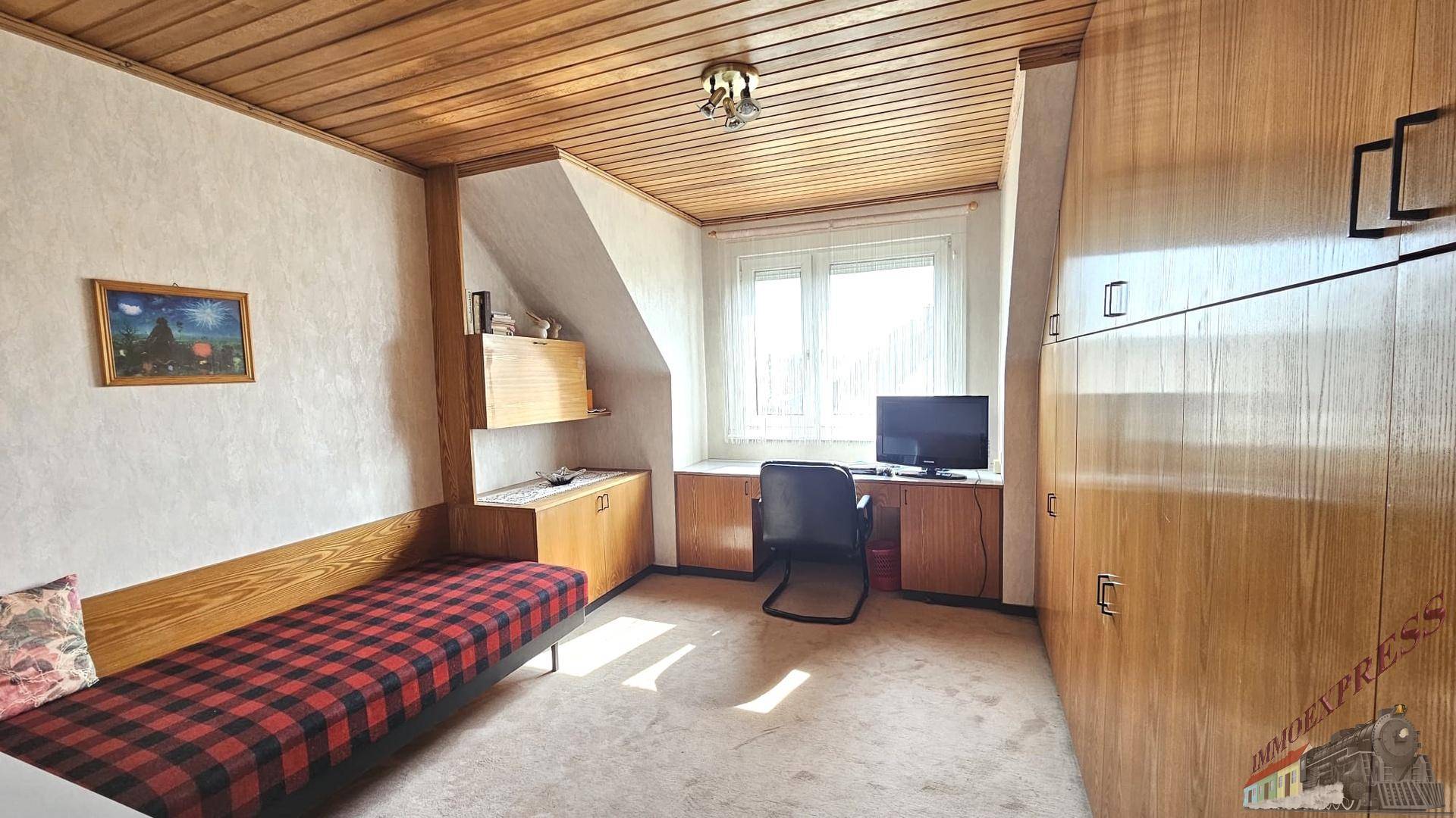 Helles Schlafzimmer mit Holzdecke, Einzelbett und Schreibtisch unter einer Dachschräge.