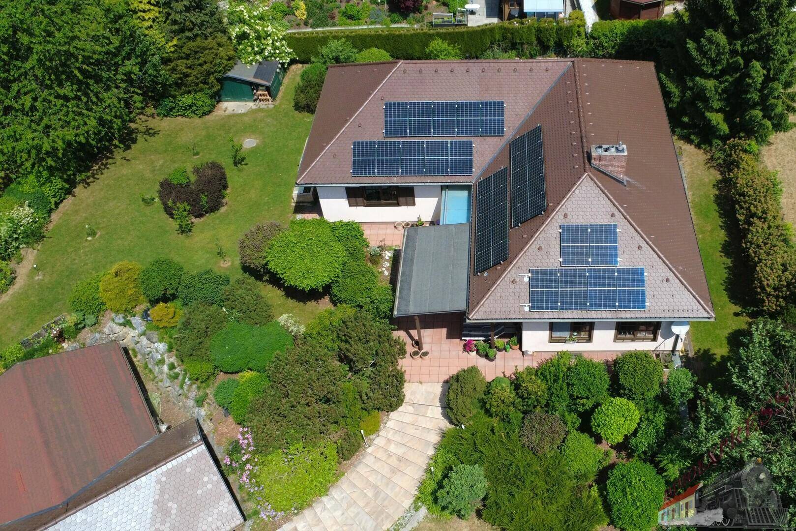 Vogelperspektive des Hauses mit Solaranlagen auf dem Dach und einem weitläufigen, grünen Garten.