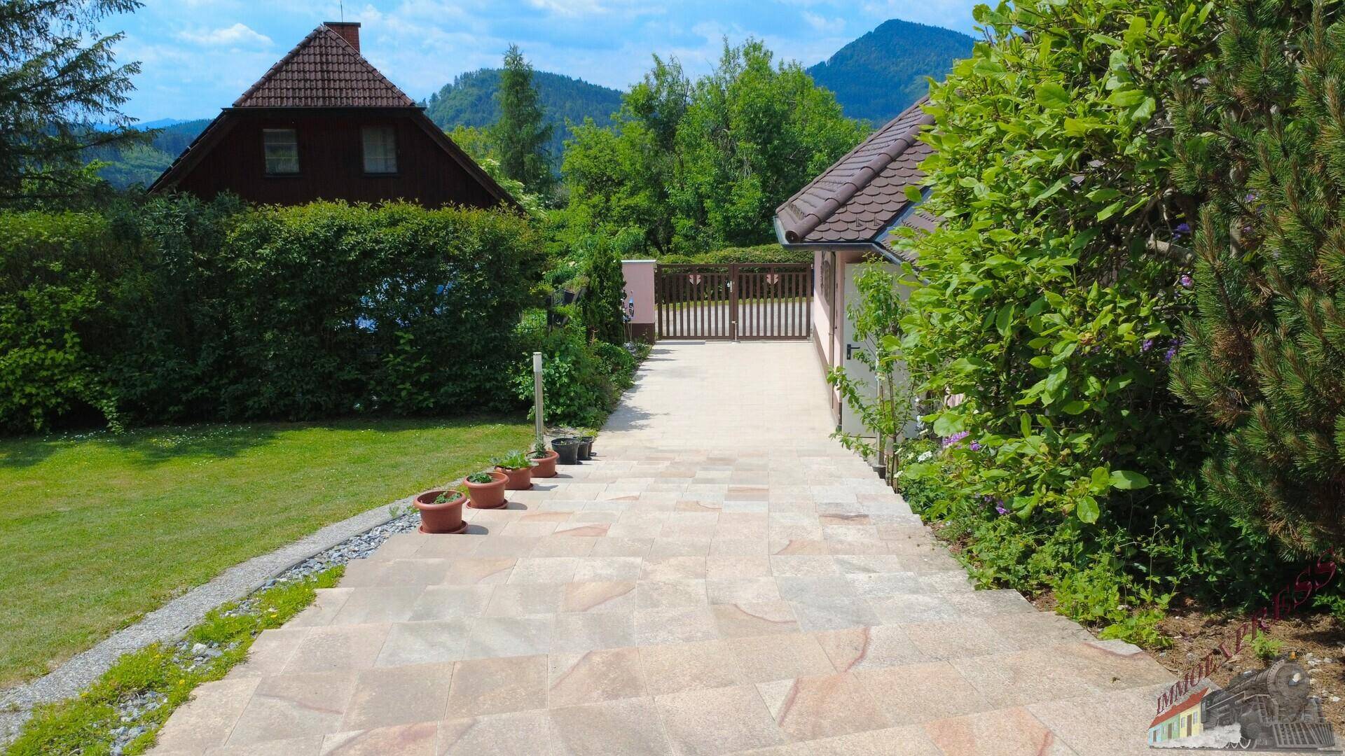 Geschwungener Steinweg führt zum Haus, umgeben von grüner Hecke und mit Bergblick im Hintergrund.