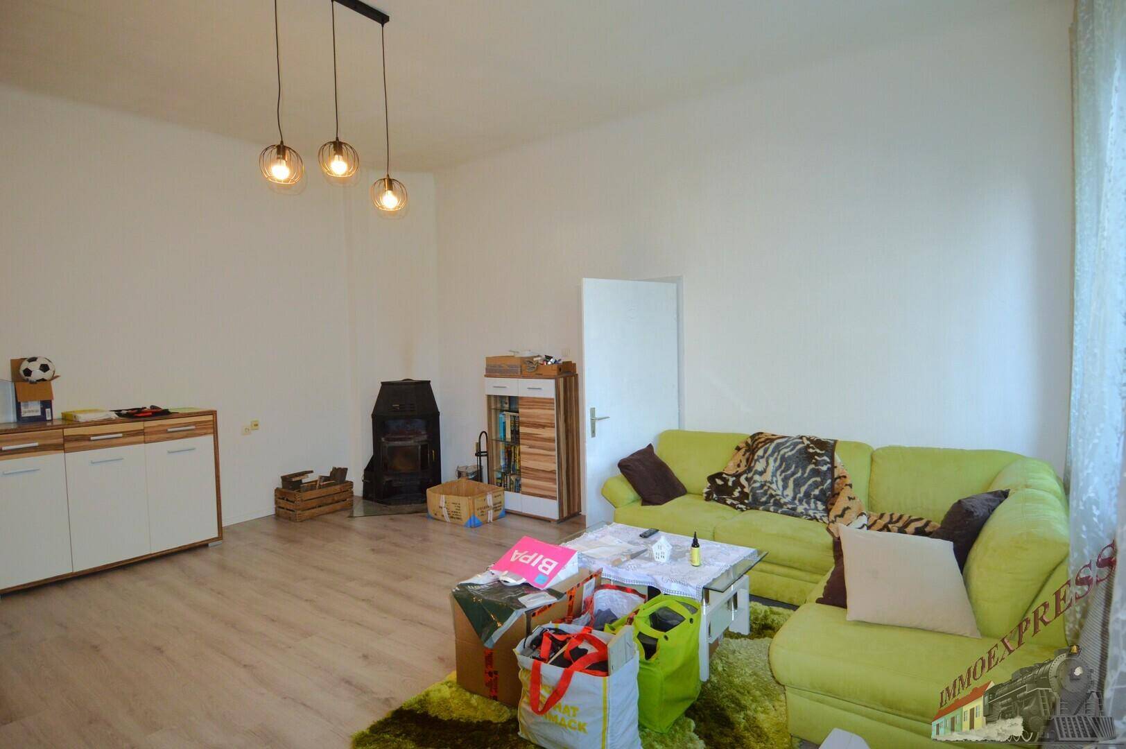 Helles Wohnzimmer mit grünem Sofa, Kaminofen und Laminatboden.