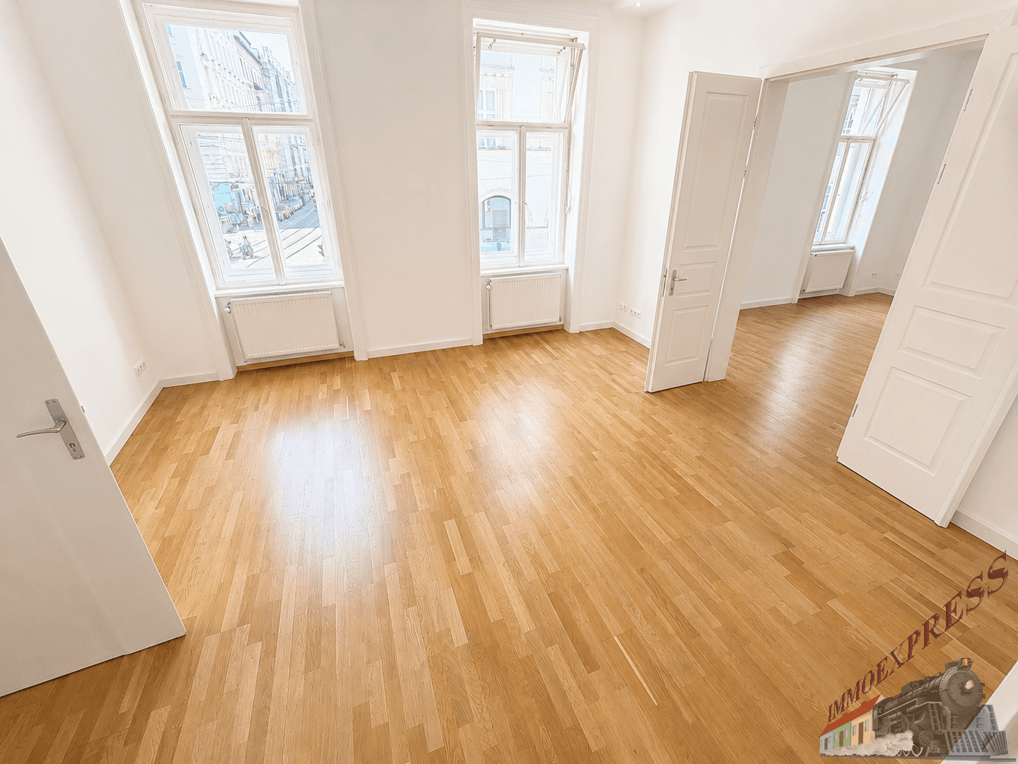 Geräumiges Zimmer mit Parkettboden, hohen Fenstern und Zugang zu weiteren Räumen, typisch für Altbau.