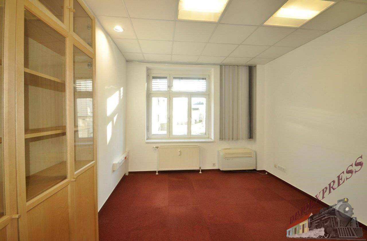 Büro mit Teppichboden, Fenster, Heizkörper und einem Holzregal an der Seitenwand.