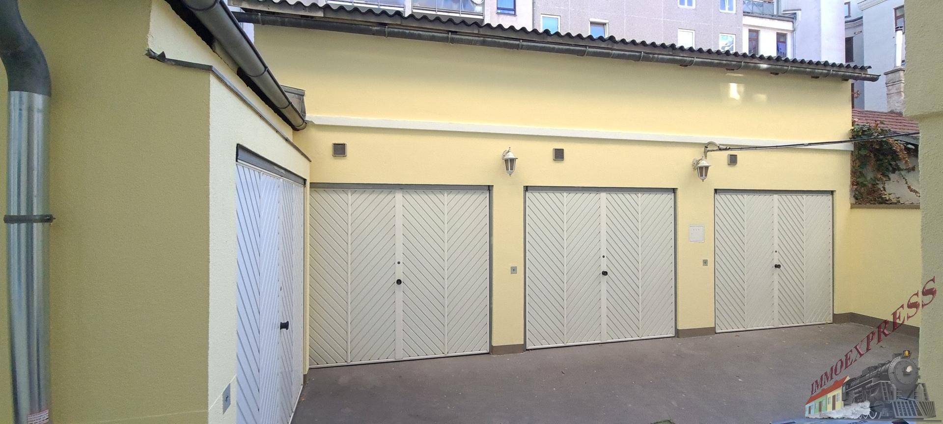 Mehrere Garagentore an einem gelben Gebäude mit einem gepflasterten Vorplatz.