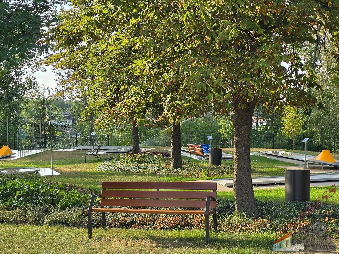 Gepflegte Minigolfanlage mit grünen Bahnen, schattenspendenden Bäumen und Sitzgelegenheiten.