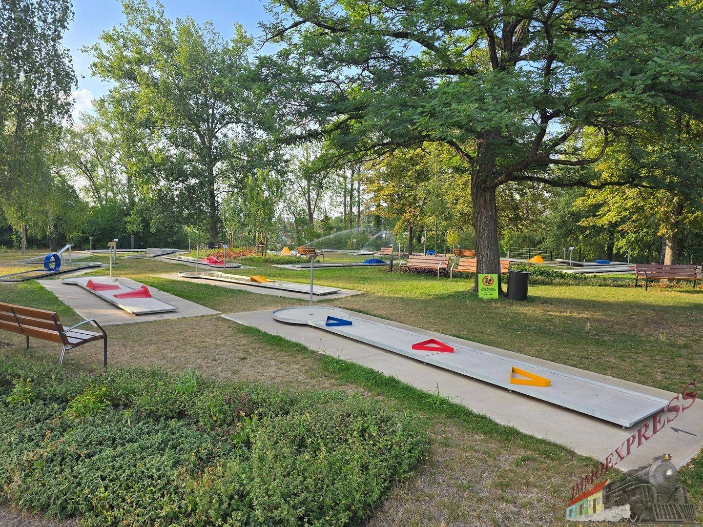 Weitläufige Minigolfanlage mit verschiedenen Bahnen, umgeben von Bäumen und bewässertem Rasen.