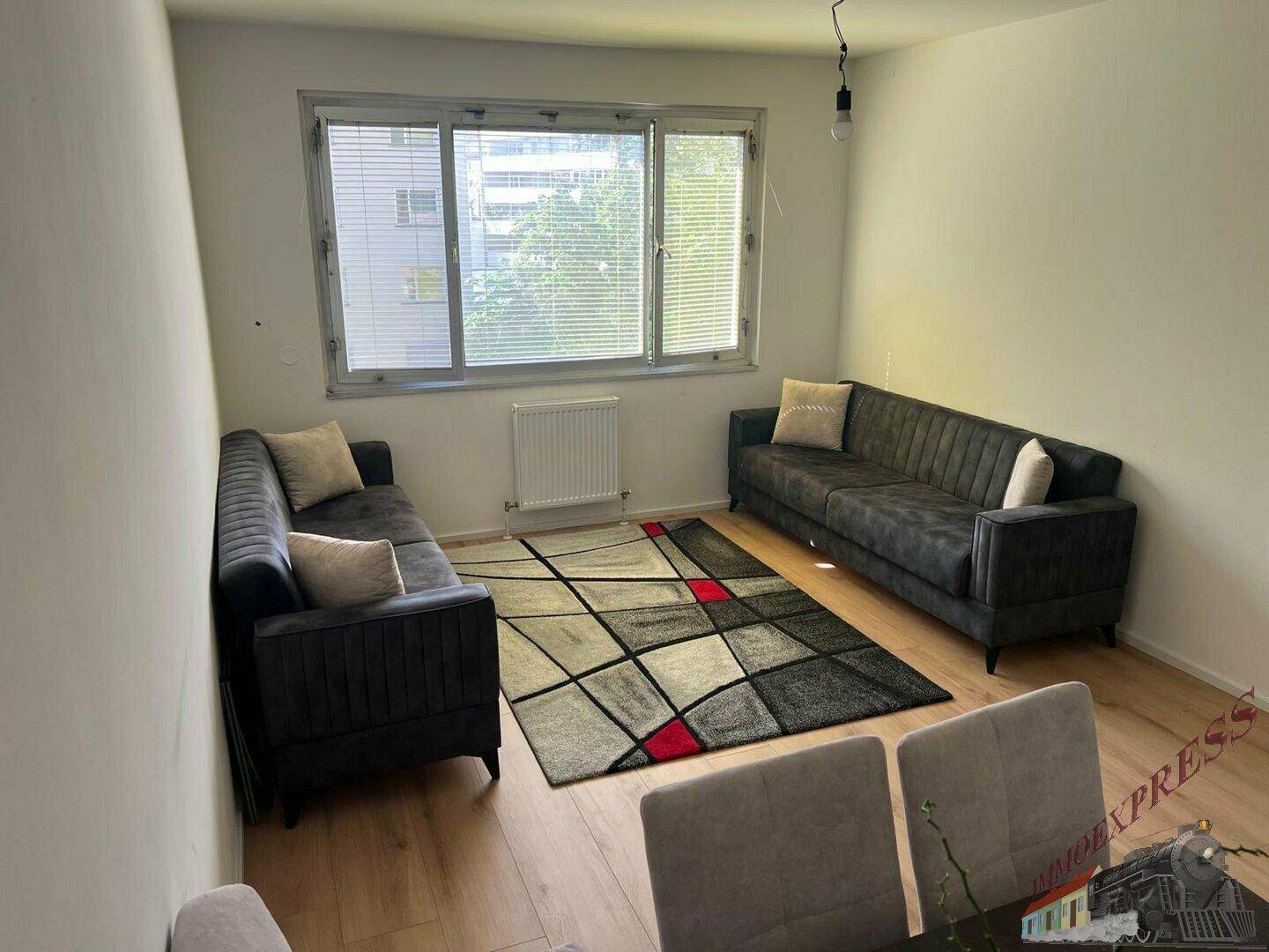 Heller Wohn- und Essbereich mit zwei Sofas, einem farbigen Teppich und großem Fenster.