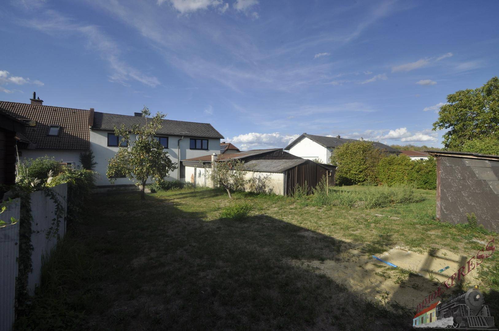 Weitläufiger Gartenbereich hinter dem Haus mit Rasenfläche und mehreren kleinen Nebengebäuden.