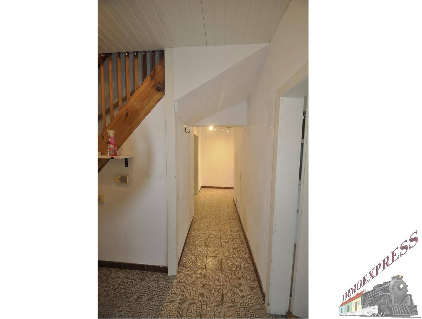 Flur mit gefliestem Boden, Holztreppe und Zugang zu weiteren Räumen.