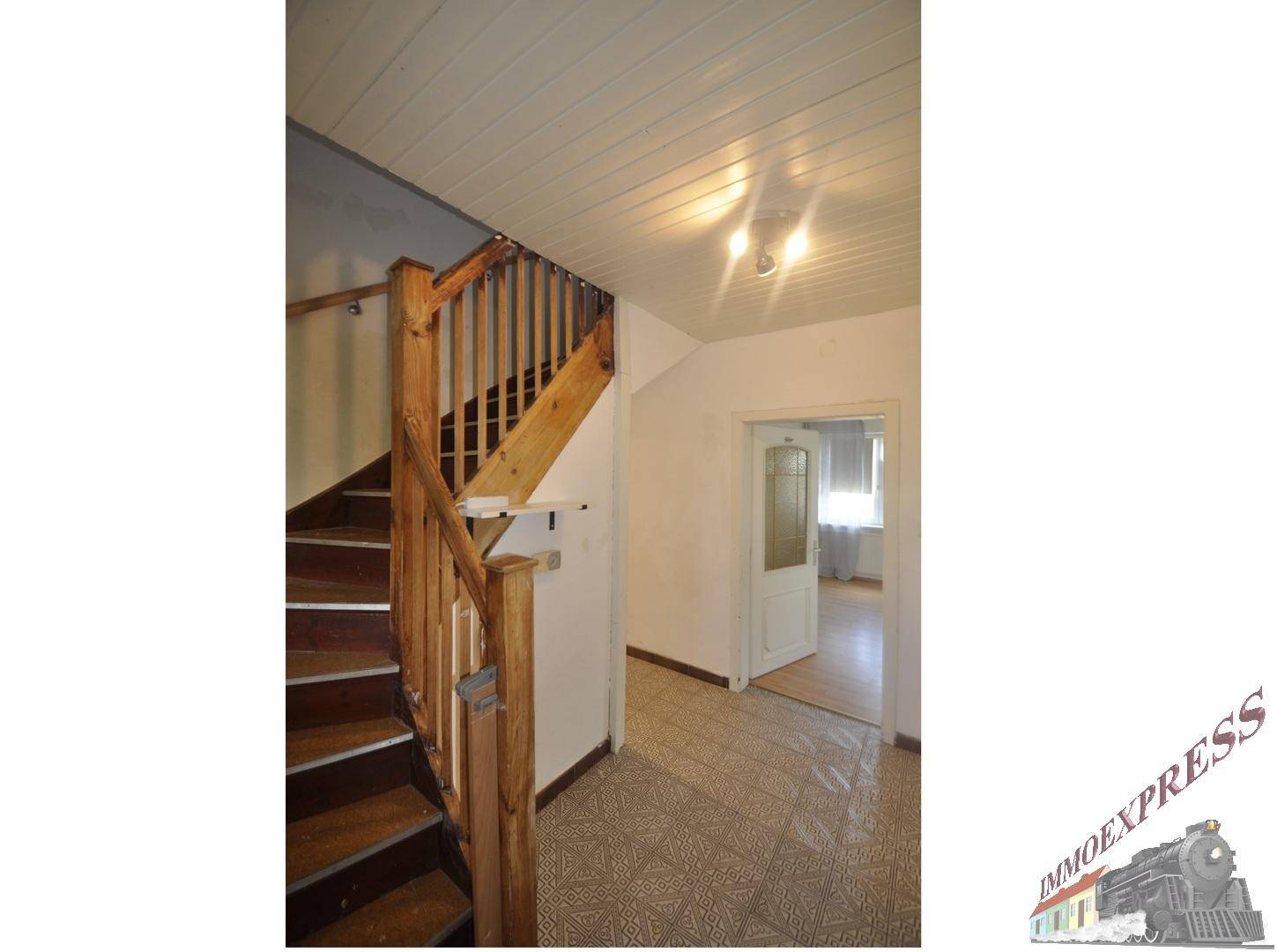 Flur mit Holztreppe, gefliestem Boden und Blick auf eine Tür zu einem weiteren Zimmer.