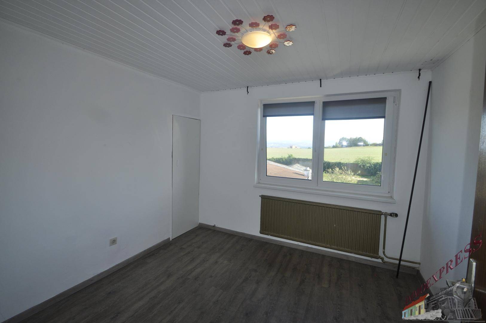 Schlafzimmer mit dunklem Laminatboden, weißer Decke und weitem Blick ins Grüne.