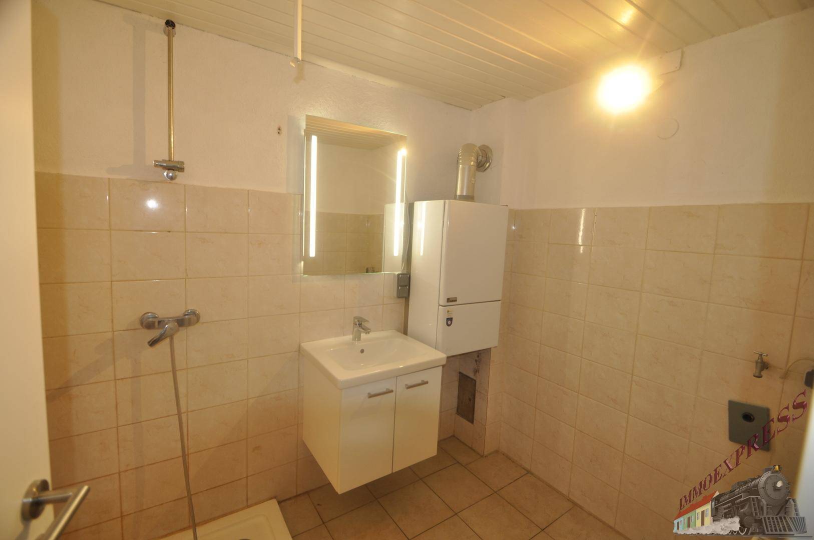 Badezimmer mit Dusche, Waschbecken, Spiegel und hellen Fliesen.