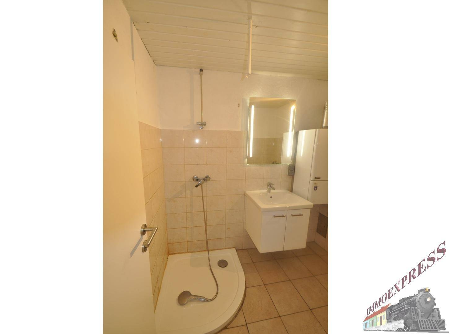 Einfaches Badezimmer mit Duschkabine, Waschbecken und Wandspiegel, ausgestattet mit Fliesen und Holzdecke.