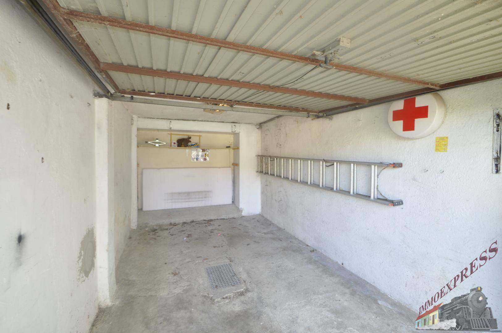 Leere Garage mit Wellblechdecke, einer Leiter an der Wand und einem Erste-Hilfe-Zeichen.