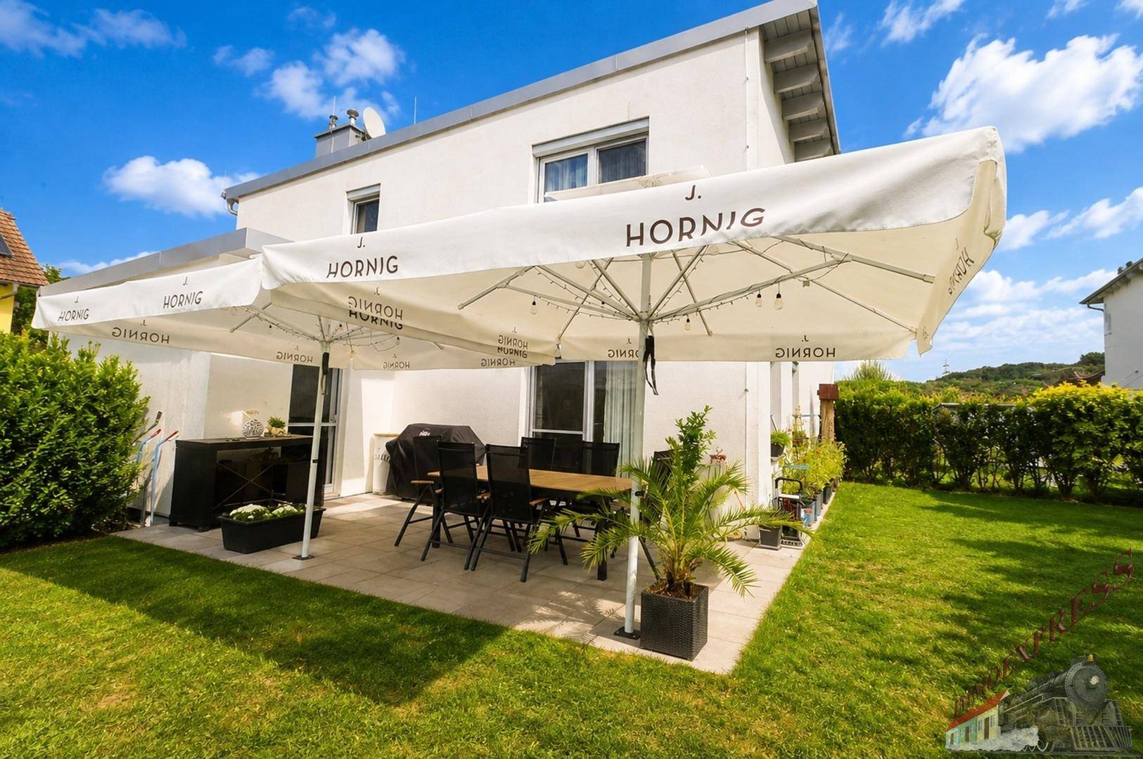Geräumige Terrasse mit großem Sonnenschirm und Gartenmöbeln neben dem Haus.