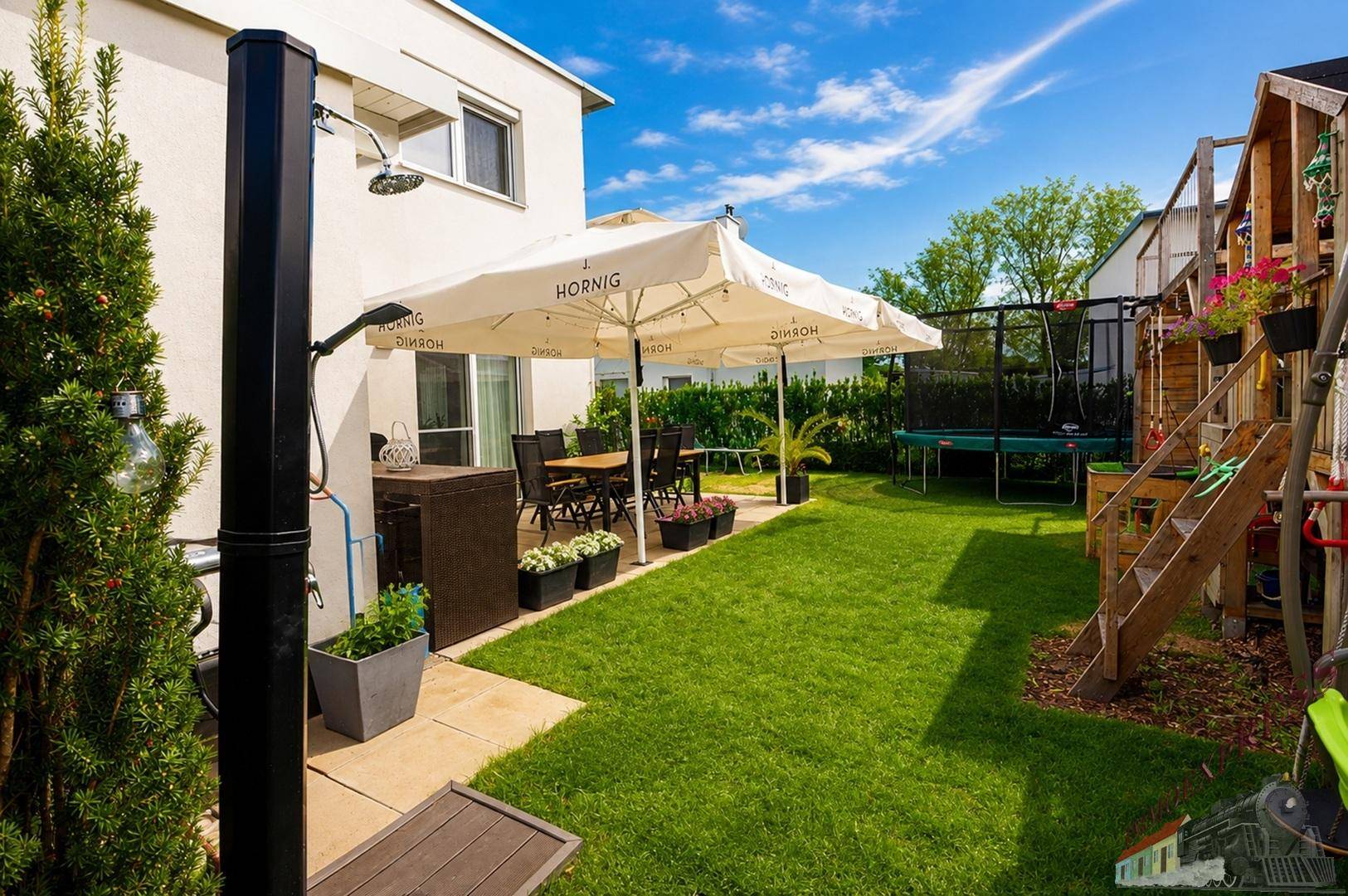 Grüner Garten mit Trampolin, Spielgerüst und Außendusche neben der Terrasse.