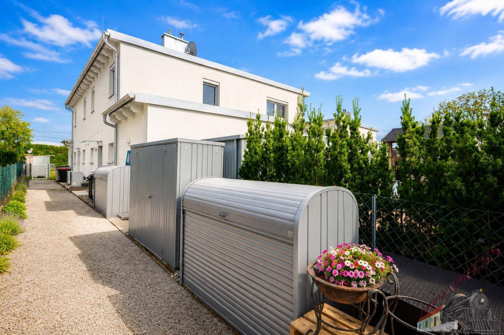Seitenansicht des Hauses mit praktischen Gartenboxen und einem Kiesweg.