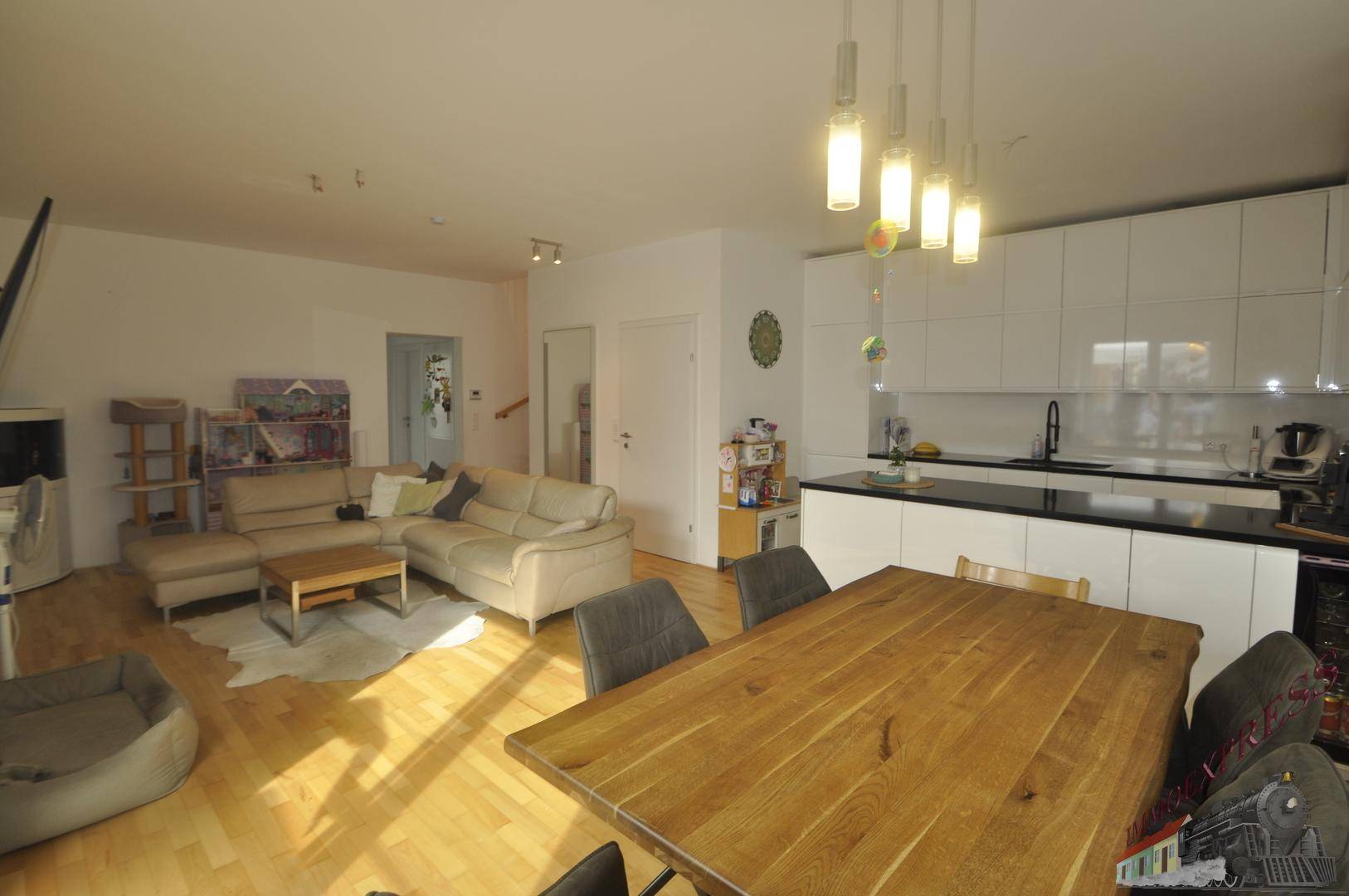 Geräumiger Wohn-Essbereich mit großem Holztisch und integrierter, moderner Küche.