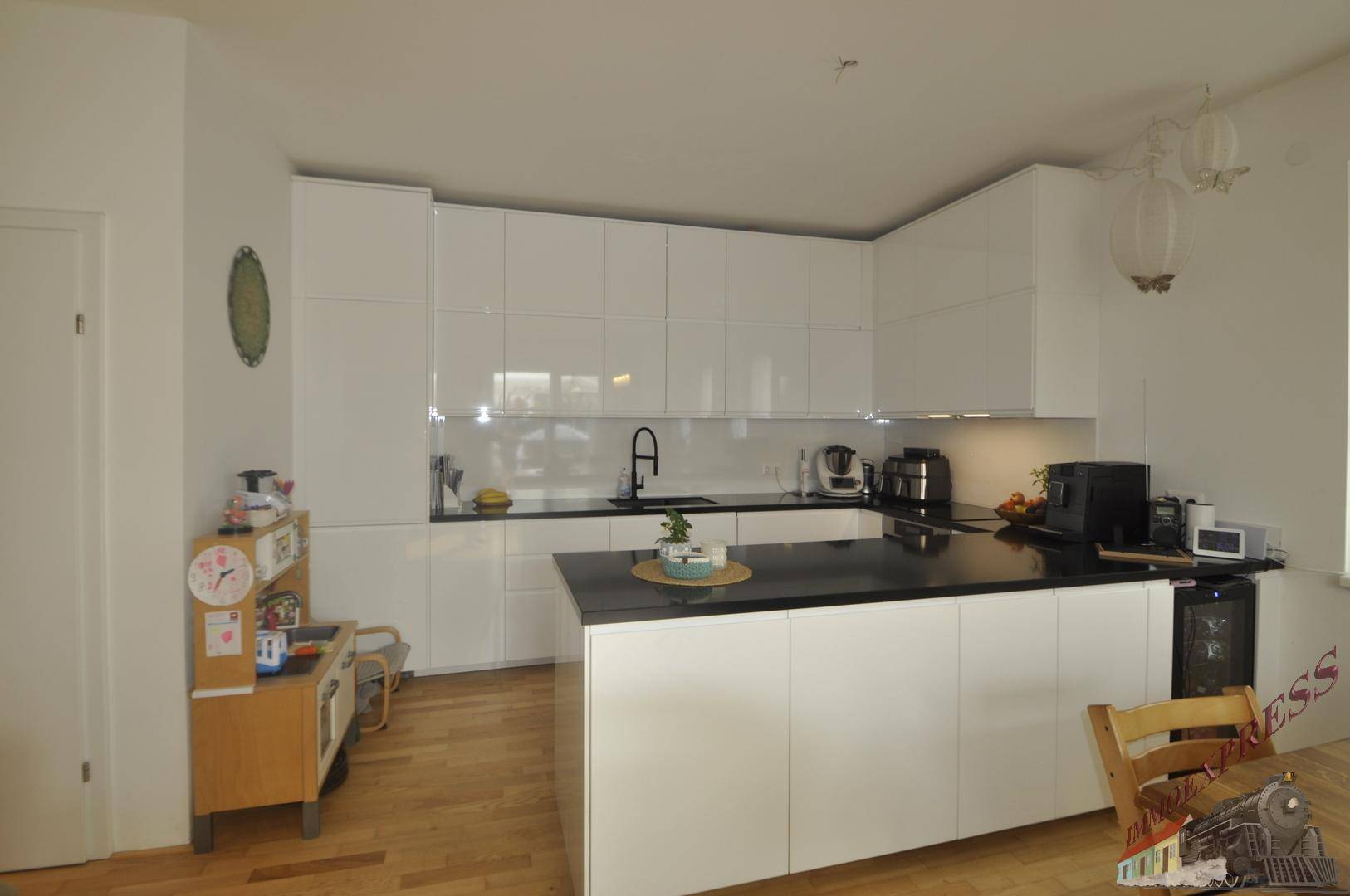 Moderne Einbauküche mit weißen Hochglanzfronten, dunkler Arbeitsplatte und Kücheninsel.